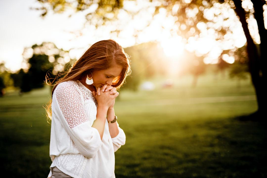 Woman clasping hands, maybe to pray with sun setting